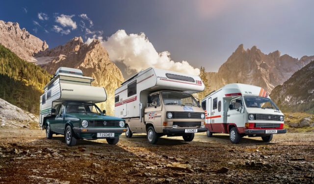 Drei klassische Tischer-Kabinen auf Pick-ups, geparkt vor einer alpinen Bergkulisse.