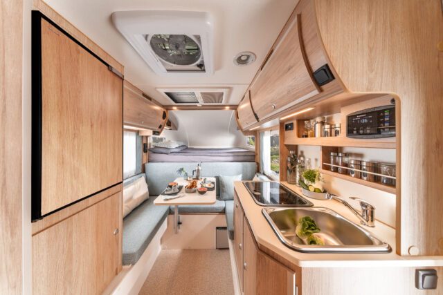 Trail230S Tischer Wohnkabine mit Küchenzeile, Oberschränken und Dinette – Blickrichtung zum Alkovenbett.