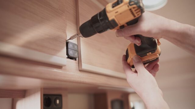 tischer_manufaktur_Hand mit Akkuschrauber montiert Steckdose in Möbelmodul.